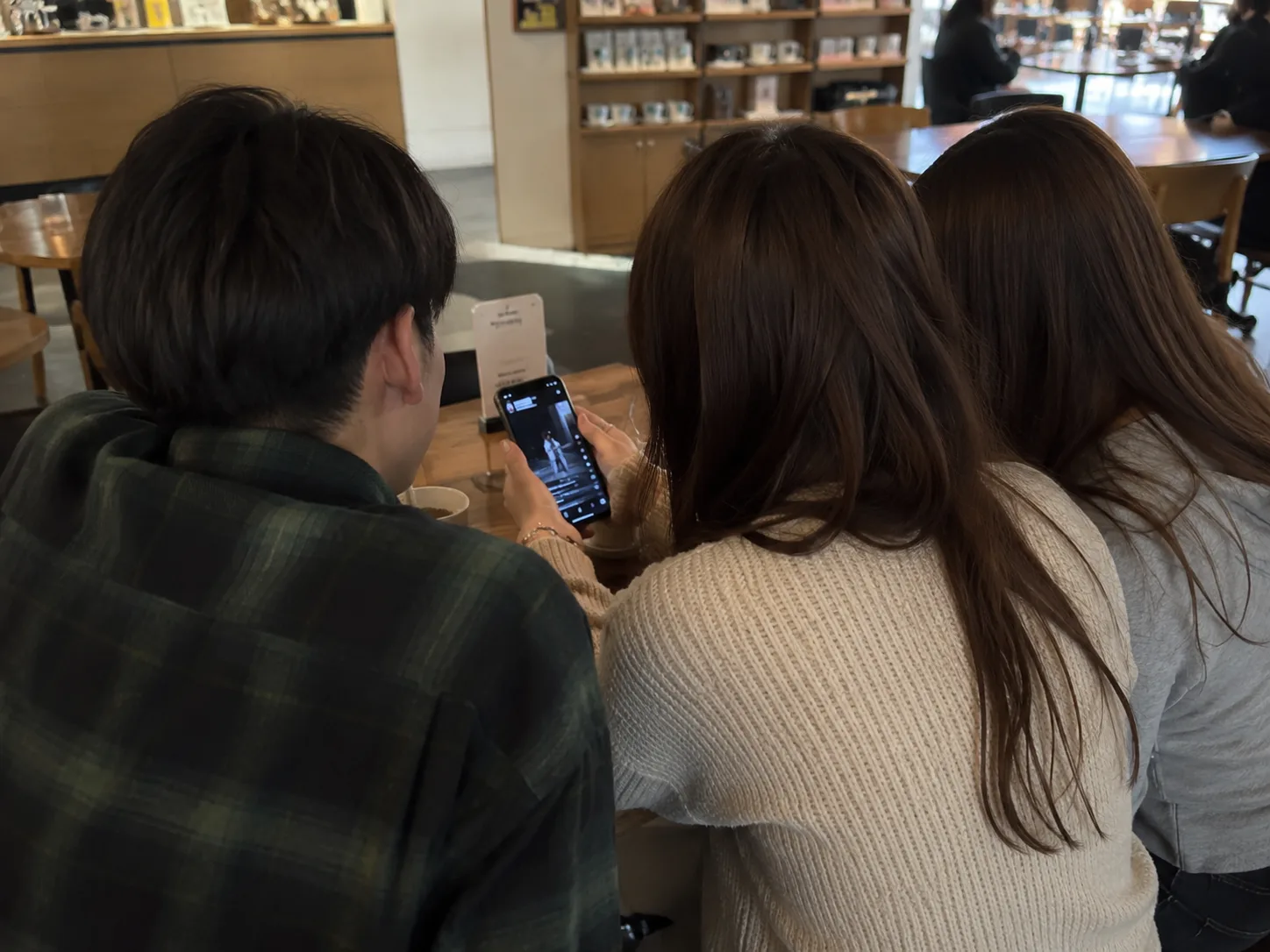 カフェで若者たちがスマホを囲み、知らないアーティストの練習クリップに見入っている
